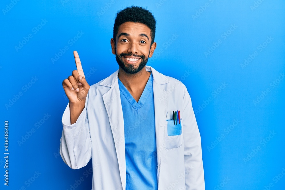 Handsome hispanic man with beard wearing doctor uniform showing and pointing up with finger number one while smiling confident and happy. Handsome hispanic man with beard wearing doctor uniform showing and pointing up with finger number one while smiling confident and happy.