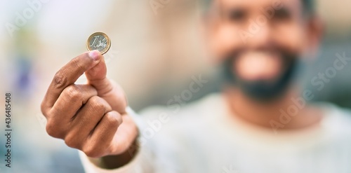 Young african american man smiling happy showing 1 euro coin at the city.
