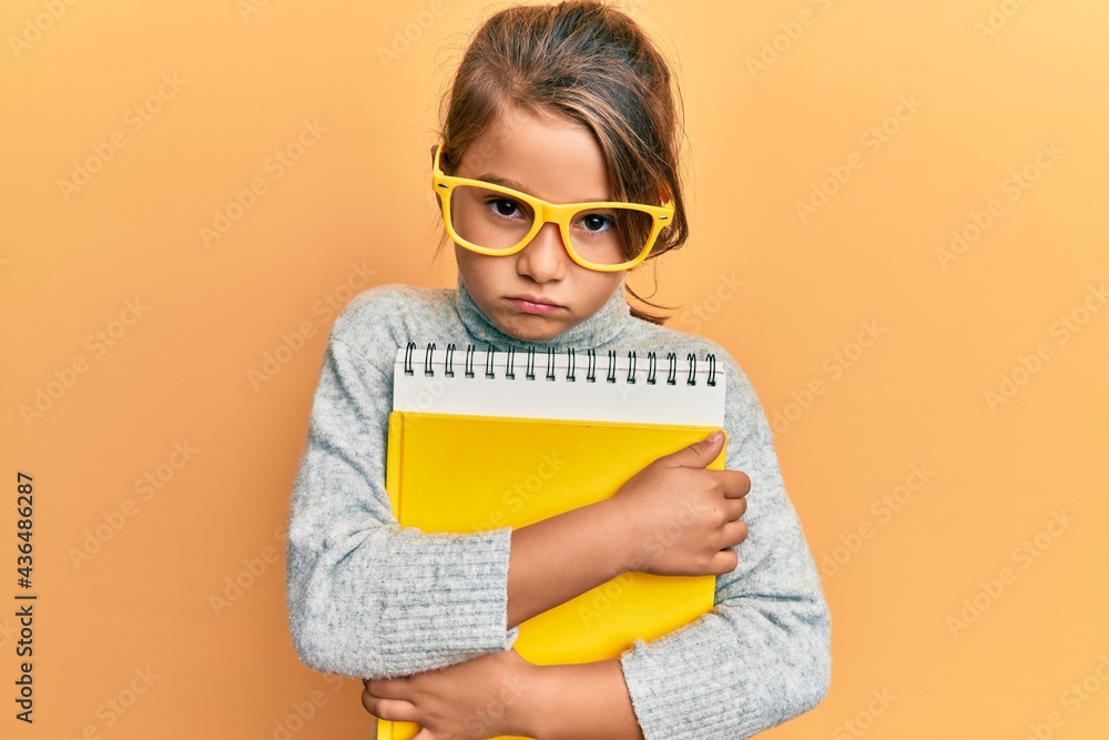 Little beautiful girl wearing glasses and holding books skeptic and nervous, frowning upset because of problem. negative person. Little beautiful girl wearing glasses and holding books skeptic and nervous, frowning upset because of problem. negative person.