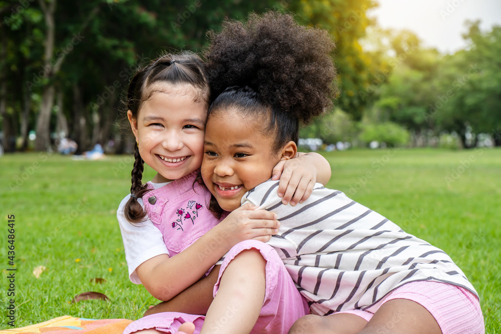 Two African American cheerful little girl sitting on the mat and hugging each other with love in the garden Two African American cheerful little girl sitting on the mat and hugging each other with love in the garden