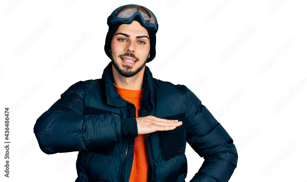 Young hispanic man with beard wearing snow wear and sky glasses gesturing with hands showing big and large size sign, measure symbol. smiling looking at the camera. measuring concept. Young hispanic man with beard wearing snow wear and sky glasses gesturing with hands showing big and large size sign, measure symbol. smiling looking at the camera. measuring concept.