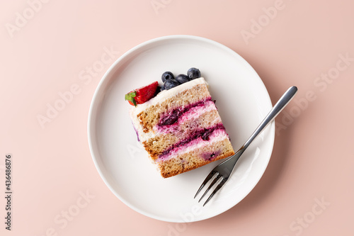 slice of blueberry cake decorated with fresh berries on white plate. delicious layered cake. pink background. top view