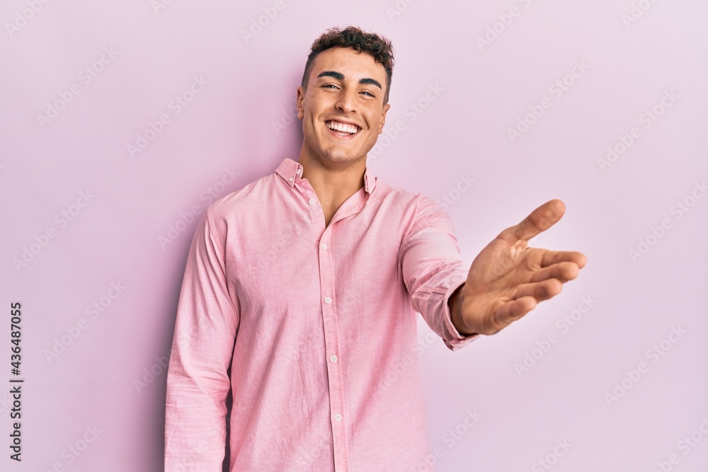 Hispanic young man wearing casual clothes smiling friendly offering handshake as greeting and welcoming. successful business. Hispanic young man wearing casual clothes smiling friendly offering handshake as greeting and welcoming. successful business.