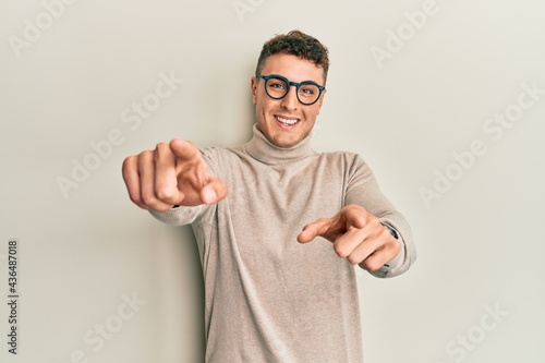Hispanic young man wearing casual turtleneck sweater pointing to you and the camera with fingers, smiling positive and cheerful © Krakenimages.com
