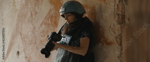 CU Portrait of Caucasian female war journalist wearing protective helmet and bulletproof vest gear taking photos under fire. Shot with 2x anamorphic lens photo