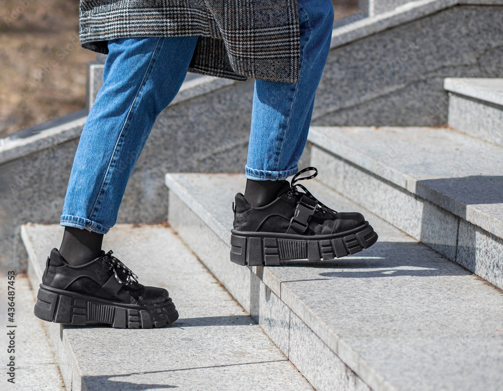 A girl in massive black boots, jeans and a checkered coat climbs up the granite stairs A girl in massive black boots, jeans and a checkered coat climbs up the granite stairs
