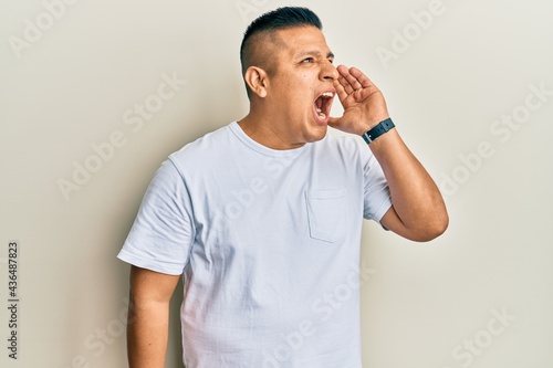 Young latin man wearing casual white t shirt shouting and screaming loud to side with hand on mouth. communication concept.