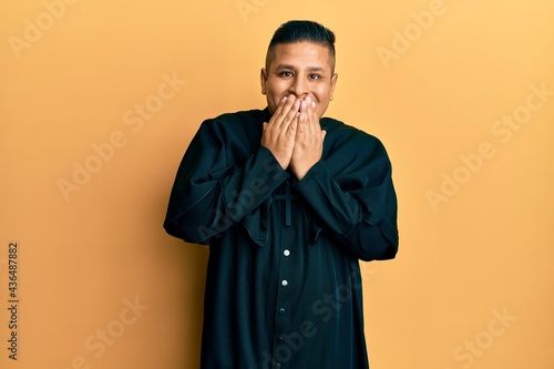 Foto Young latin priest man standing over yellow background laughing and embarrassed