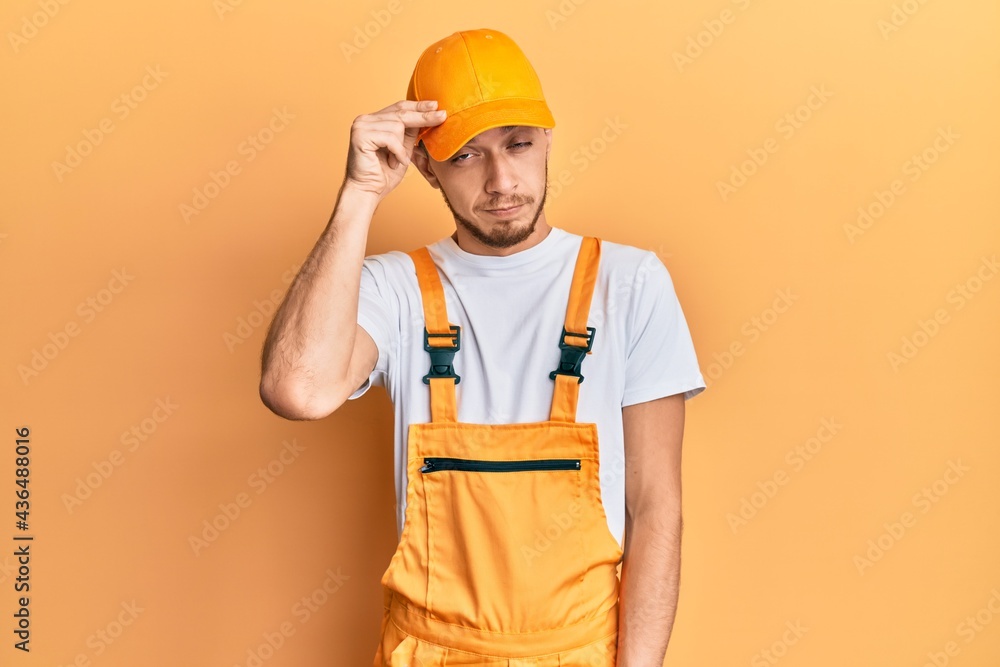 Hispanic young man wearing handyman uniform worried and stressed about a problem with hand on forehead, nervous and anxious for crisis Hispanic young man wearing handyman uniform worried and stressed about a problem with hand on forehead, nervous and anxious for crisis