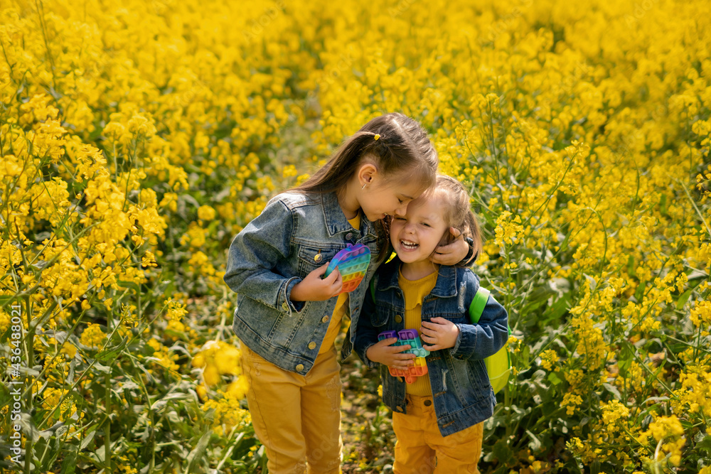Two girls in a rapeseed field tenderly embrace each other and laugh ...