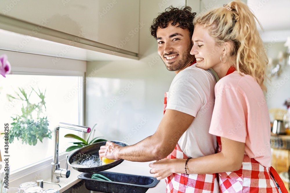 Obraz premium Young couple smiling happy and hugging washing dishes at kitchen.