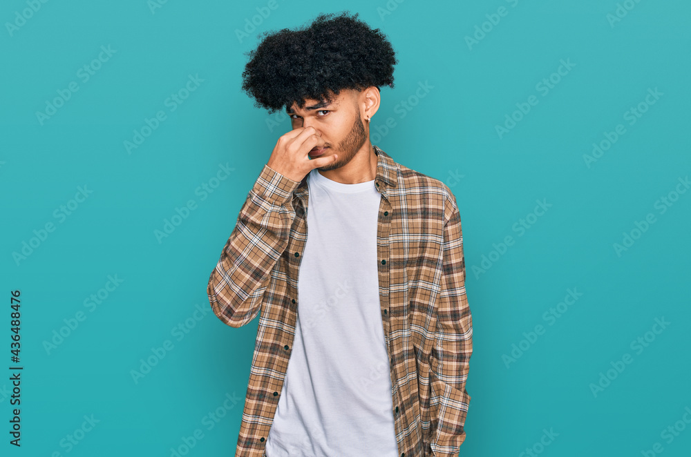 Young african american man with afro hair wearing casual clothes smelling something stinky and disgusting, intolerable smell, holding breath with fingers on nose. bad smell Young african american man with afro hair wearing casual clothes smelling something stinky and disgusting, intolerable smell, holding breath with fingers on nose. bad smell