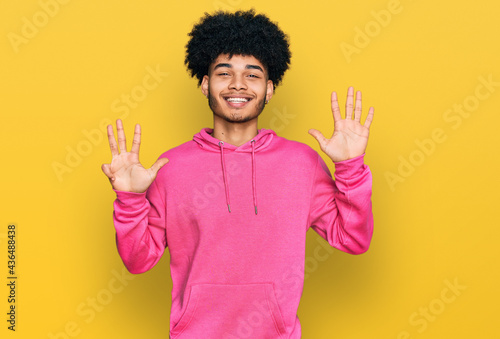 Young african american man with afro hair wearing casual pink sweatshirt showing and pointing up with fingers number nine while smiling confident and happy.