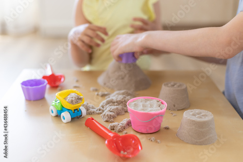 Kinetic sand of natural color with toys on table and playing children in blurred background. Creative play for kids concept. selective focus