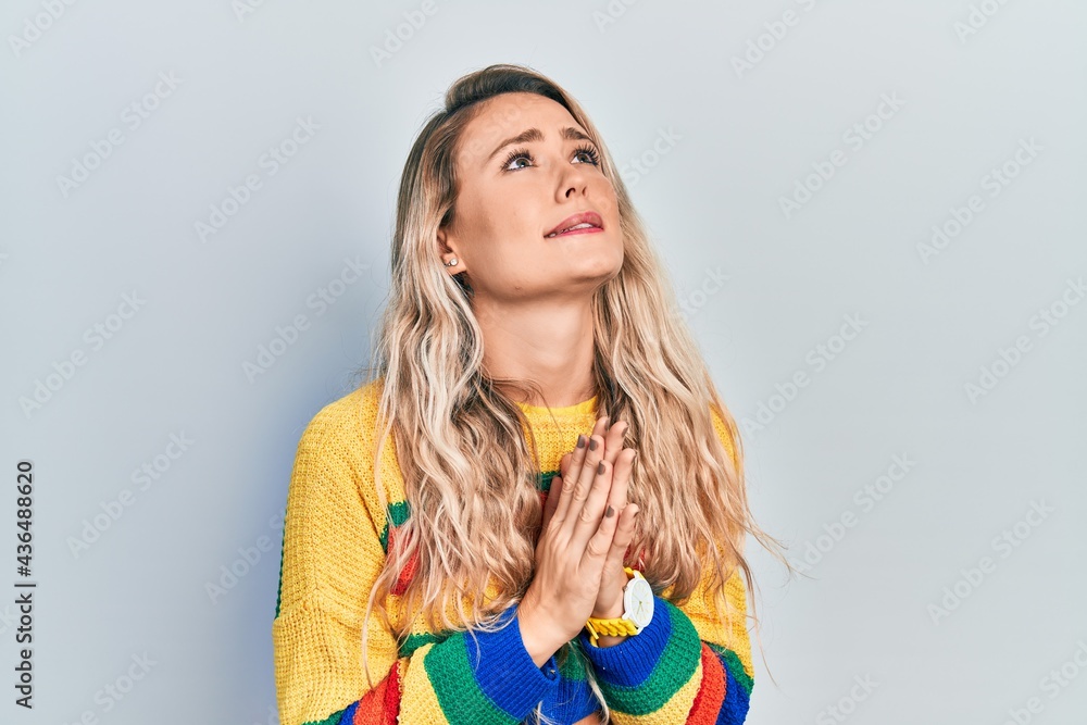 Beautiful young blonde woman wearing colored sweater begging and praying with hands together with hope expression on face very emotional and worried. begging. Beautiful young blonde woman wearing colored sweater begging and praying with hands together with hope expression on face very emotional and worried. begging.