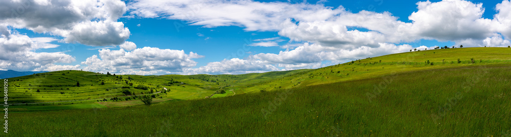 Fototapeta premium Panoramic scenic view of green hills at springtime, blue sky with white clouds in Transylvania, Romania.