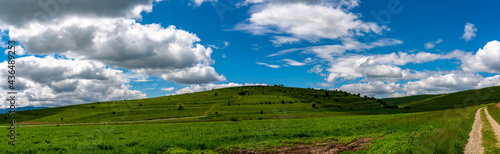 Panoramic view, green hills , terraced agricultural fields near dirt road , blue sky with white clouds background.
