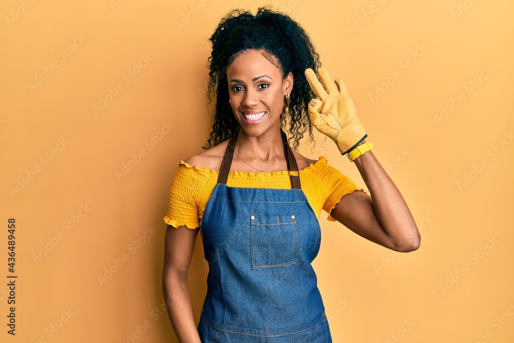 Middle age african american woman wearing professional apron smiling positive doing ok sign with hand and fingers. successful expression. Middle age african american woman wearing professional apron smiling positive doing ok sign with hand and fingers. successful expression.