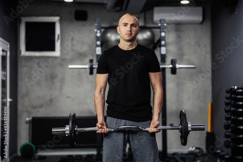 Proper posture before performing exercises. A man in sportswear pumps his arm muscles and lifts a barbell with the weights plate with both hands in a modern gym. A close-up shot of a male person