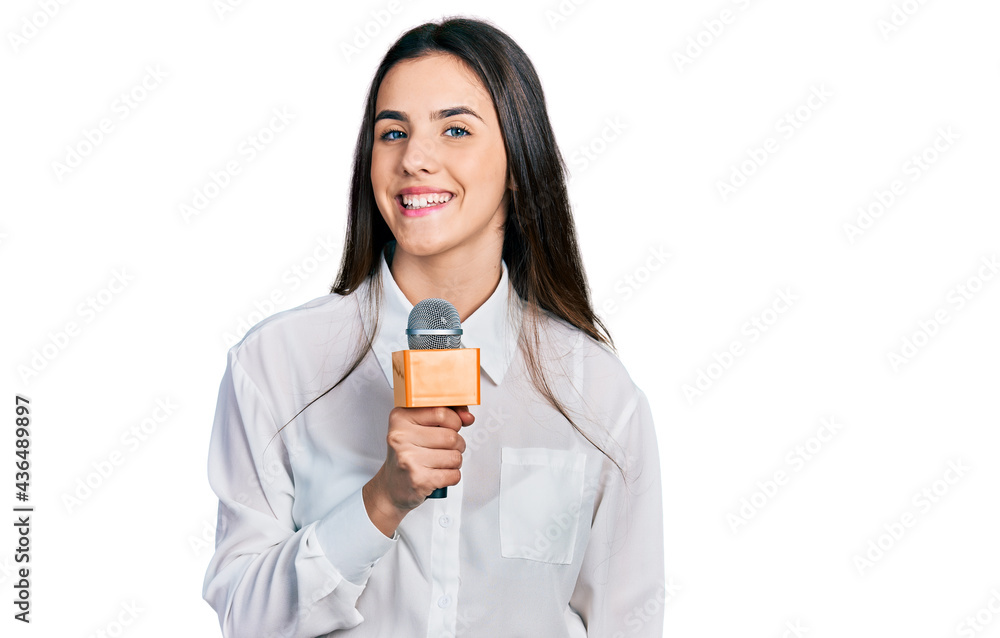 Young brunette teenager holding reporter microphone looking positive and happy standing and smiling with a confident smile showing teeth Young brunette teenager holding reporter microphone looking positive and happy standing and smiling with a confident smile showing teeth