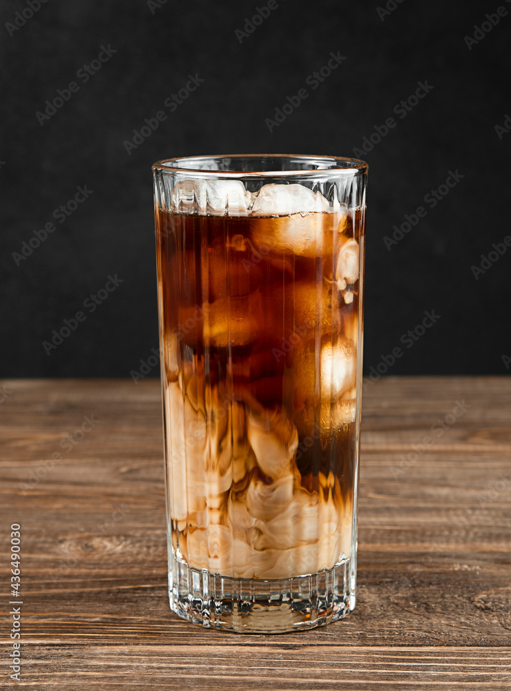 Iced coffee with ice and cream in a tall glass close-up on a dark wooden background. Iced coffee with ice and cream in a tall glass close-up on a dark wooden background.