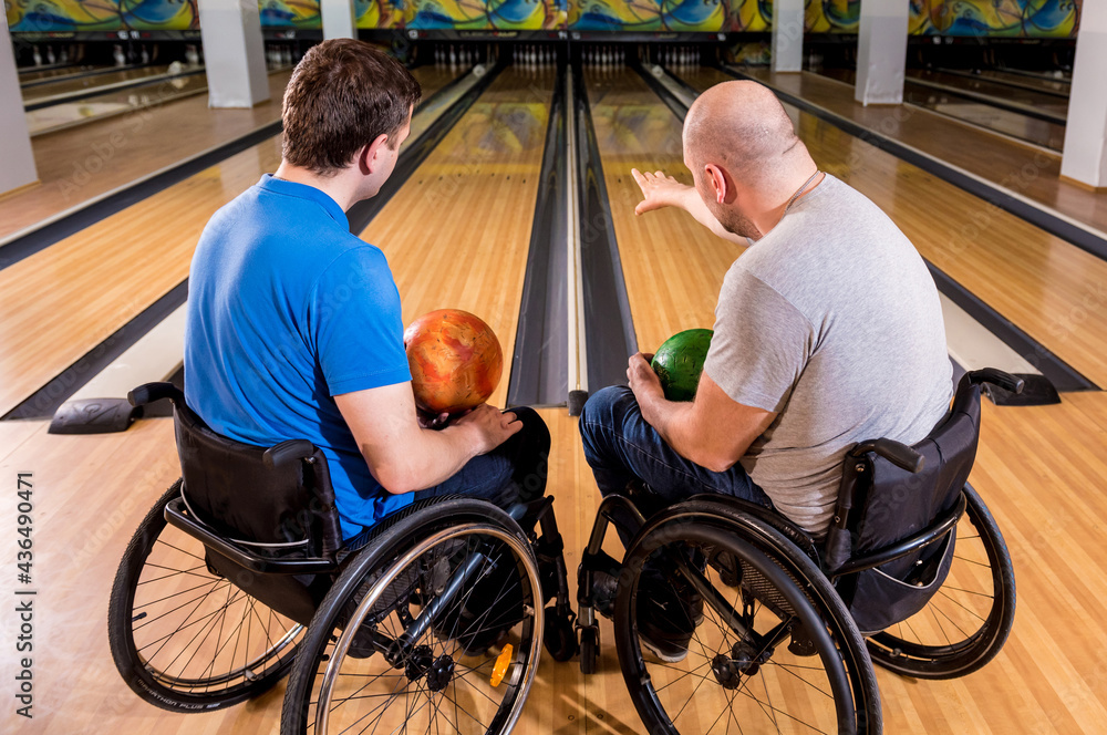 Two young disabled men in wheelchairs playing bowling in the club Two young disabled men in wheelchairs playing bowling in the club