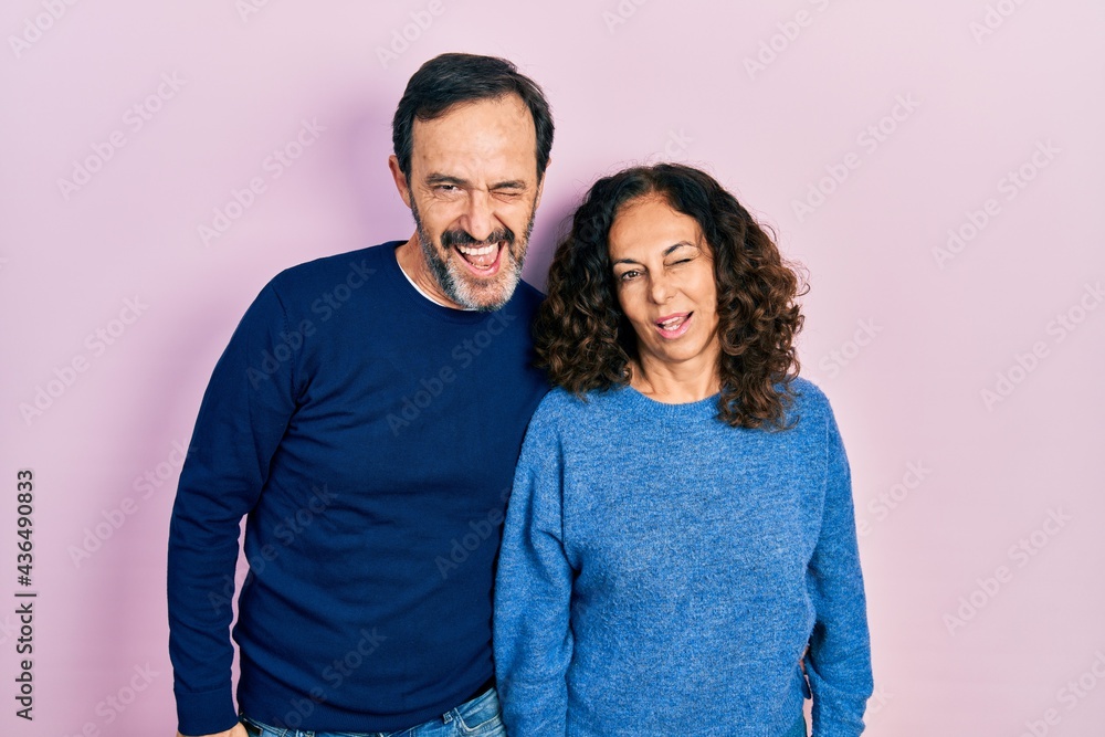 Middle age couple of hispanic woman and man hugging and standing together winking looking at the camera with sexy expression, cheerful and happy face.