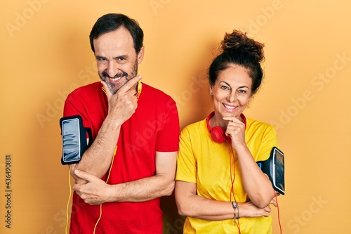 Middle age couple of hispanic woman and man wearing sportswear and arm band looking confident at the camera smiling with crossed arms and hand raised on chin. thinking positive.