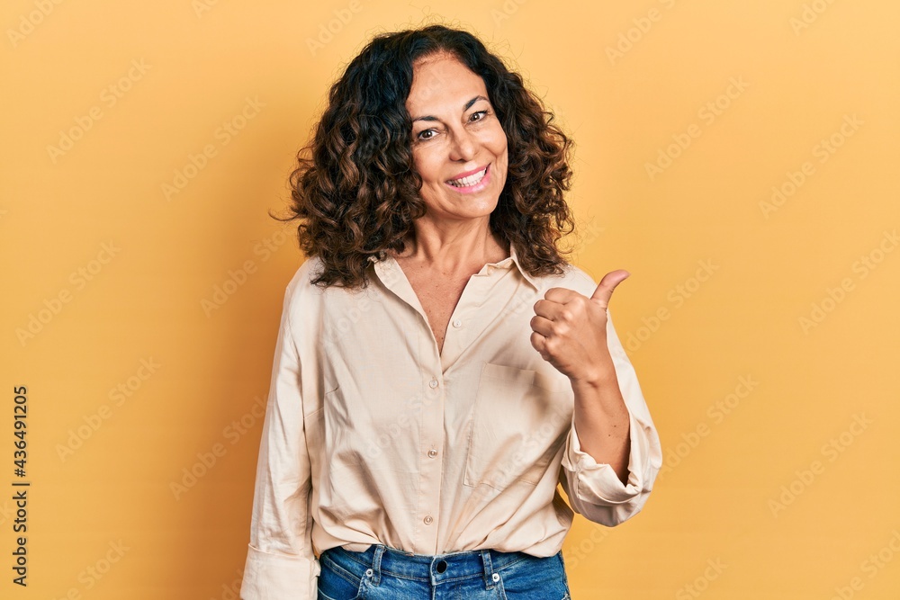 Obraz premium Middle age hispanic woman wearing casual clothes smiling with happy face looking and pointing to the side with thumb up.