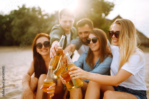 Fotografija Group of friends cheers and drink beers on the beach
