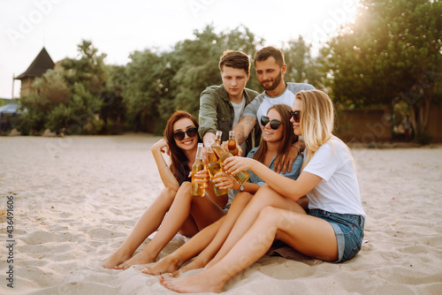 Group of friends cheers and drink beers on the beach. Young friends relaxing on the beath having picnic, toasting with beerus. People, lifestyle, travel, nature and vacations concept. photo