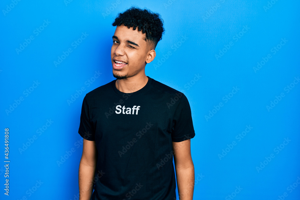 Young african american man wearing staff t shirt winking looking at the camera with sexy expression, cheerful and happy face. Young african american man wearing staff t shirt winking looking at the camera with sexy expression, cheerful and happy face.