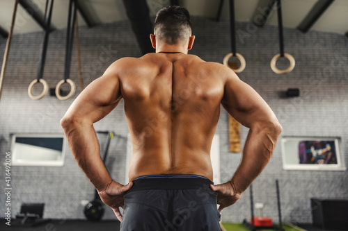 Naked muscular male back. A fitness man stands in the middle of the gym shirtless. A close-up of a muscular back from a man living a sporty life, a bare upper body. Fitness goal, no limits