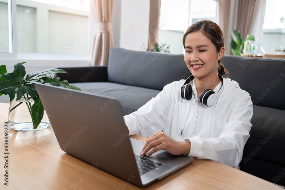 Happy casual beautiful Asian woman working on a laptop while sitting on sofa in living room at her home. Happy casual beautiful Asian woman working on a laptop while sitting on sofa in living room at her home.