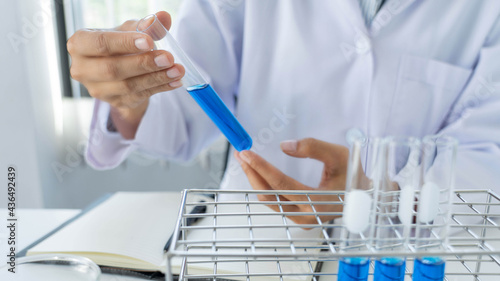 scientists researching in laboratory in white lab coat, gloves analysing, looking at test tubes sample, biotechnology concept