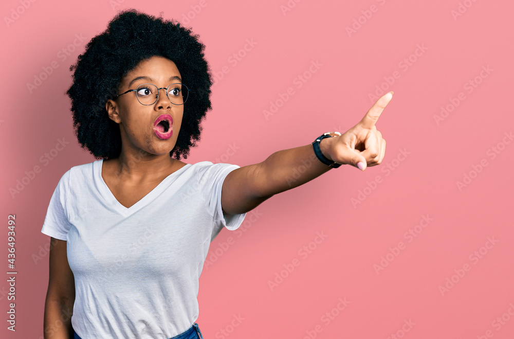 Young african american woman wearing casual white t shirt pointing with finger surprised ahead, open mouth amazed expression, something on the front Young african american woman wearing casual white t shirt pointing with finger surprised ahead, open mouth amazed expression, something on the front