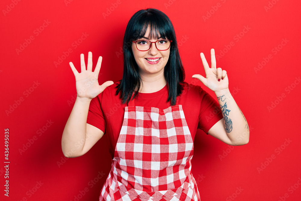 Young hispanic woman wearing cook apron and glasses showing and pointing up with fingers number eight while smiling confident and happy. Young hispanic woman wearing cook apron and glasses showing and pointing up with fingers number eight while smiling confident and happy.