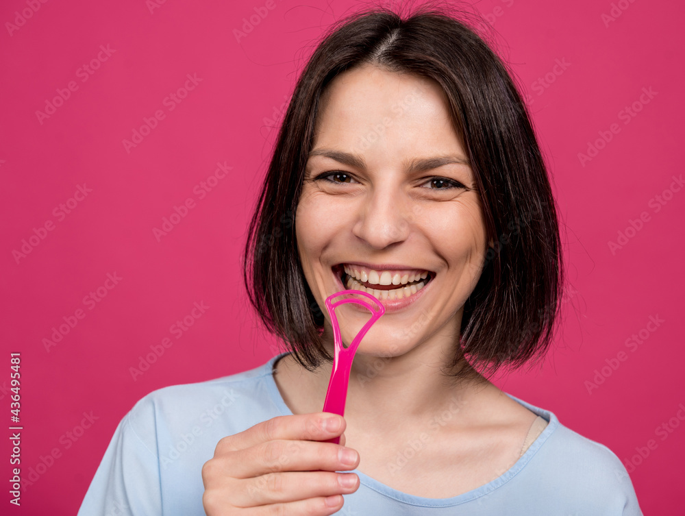 Beautiful happy young woman with tongue scraper on blank pink background Beautiful happy young woman with tongue scraper on blank pink background