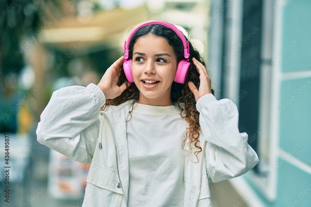 Hispanic child girl smiling happy using headphones at the city. Hispanic child girl smiling happy using headphones at the city.