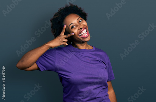 African american woman with afro hair wearing casual purple t shirt doing peace symbol with fingers over face, smiling cheerful showing victory