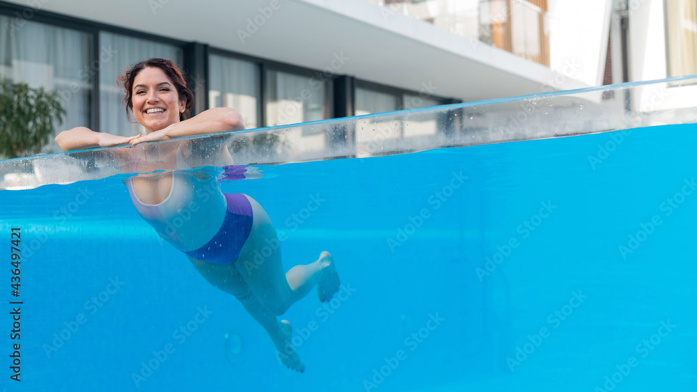 Happy caucasian woman swims in an outdoor pool with a transparent wall in a hotel