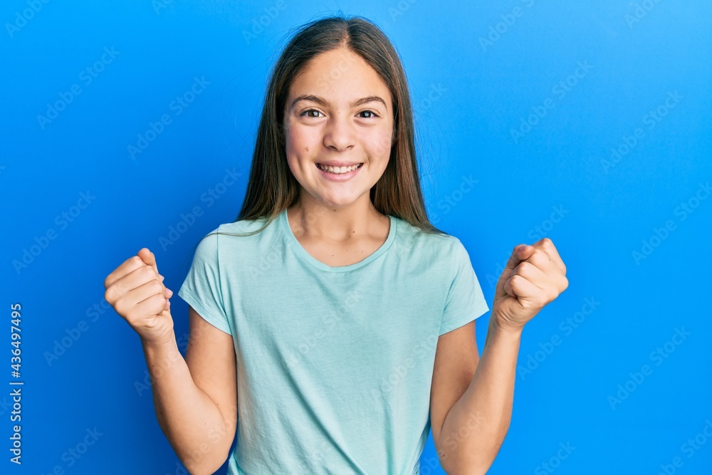 Beautiful brunette little girl wearing casual white t shirt celebrating surprised and amazed for success with arms raised and open eyes. winner concept. Beautiful brunette little girl wearing casual white t shirt celebrating surprised and amazed for success with arms raised and open eyes. winner concept.