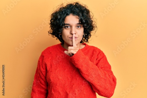 Young hispanic woman with curly hair wearing casual winter sweater asking to be quiet with finger on lips. silence and secret concept. © Krakenimages.com