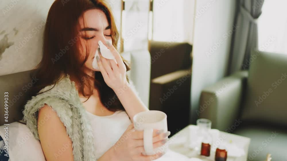 Portrait of ill  mixed race woman at home. Young woman coughing in bedroom. Close up of sick girl cough cold. Nose stuffy, sneezes and coughs. Blows nose and hides under covers.