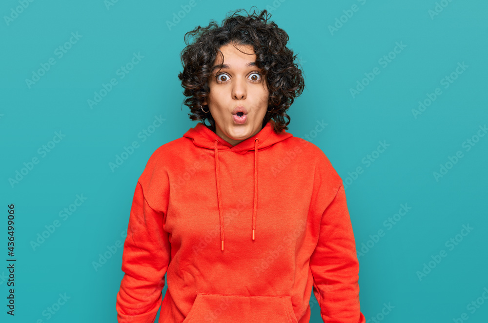 Young hispanic woman with curly hair wearing casual sweatshirt scared and amazed with open mouth for surprise, disbelief face Young hispanic woman with curly hair wearing casual sweatshirt scared and amazed with open mouth for surprise, disbelief face
