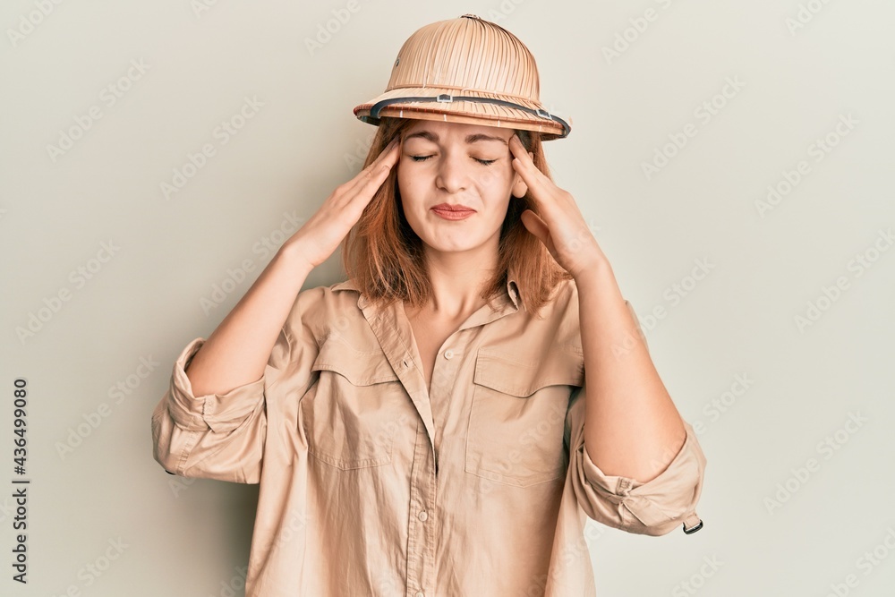 Young caucasian woman wearing explorer hat with hand on head, headache because stress. suffering migraine. Young caucasian woman wearing explorer hat with hand on head, headache because stress. suffering migraine.