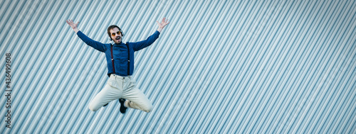 Stylish young man with headphones walks and jumps to success. Positive man, happiness, victory in life.