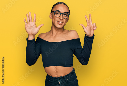 Hispanic transgender man wearing make up and long hair wearing women clothes showing and pointing up with fingers number eight while smiling confident and happy.