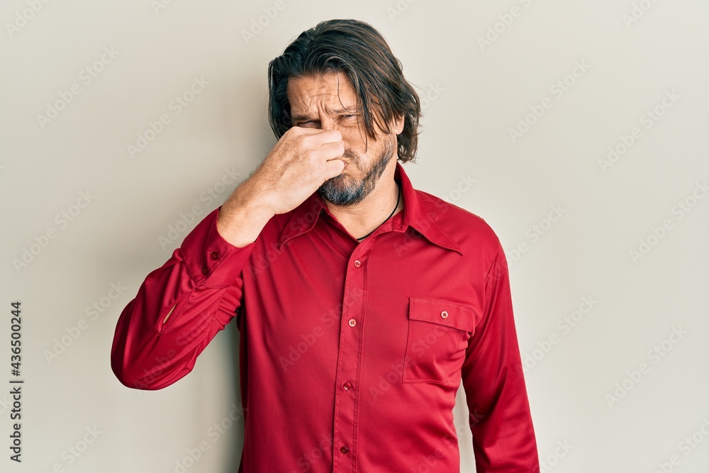Middle age handsome man wearing casual clothes smelling something stinky and disgusting, intolerable smell, holding breath with fingers on nose. bad smell Middle age handsome man wearing casual clothes smelling something stinky and disgusting, intolerable smell, holding breath with fingers on nose. bad smell