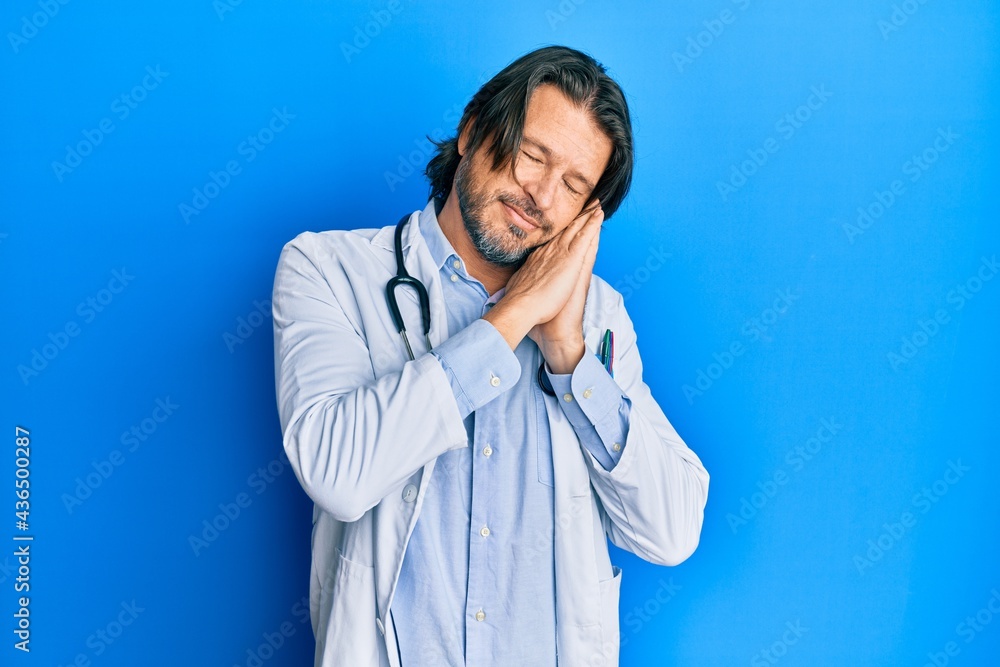 Middle age handsome man wearing doctor uniform and stethoscope sleeping tired dreaming and posing with hands together while smiling with closed eyes. Middle age handsome man wearing doctor uniform and stethoscope sleeping tired dreaming and posing with hands together while smiling with closed eyes.